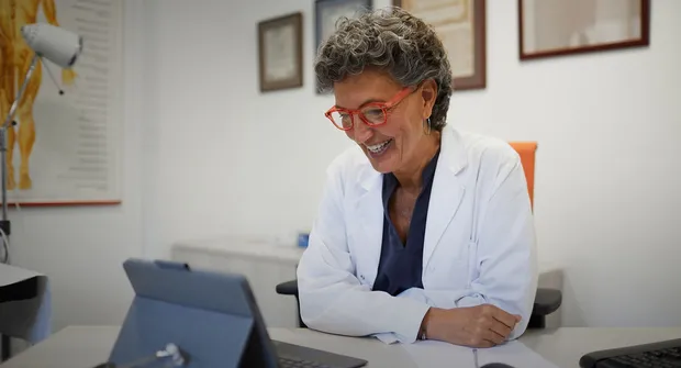 Pessoa de jaleco sorrindo em mesa de atendimento representando o SAC da AstraZeneca farmacêutica